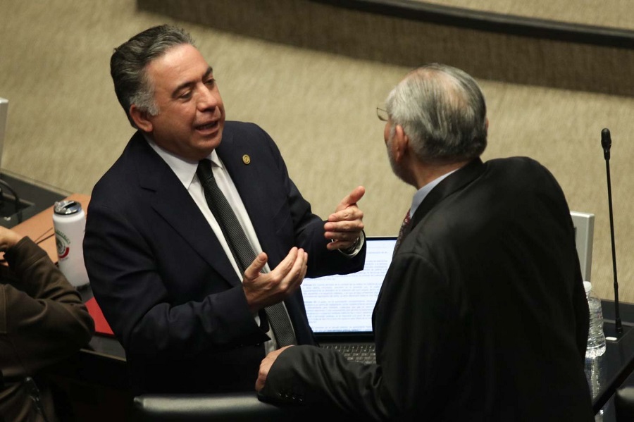 Dos hombres vestidos de traje dialogando en un parlamento.