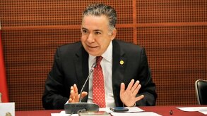 Hombre vestido de traje haciendo una seña con las manos mientras habla frente a un micrófono.