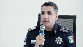 Hombre vestido con uniforme policiaco hablando ante un micrófono.