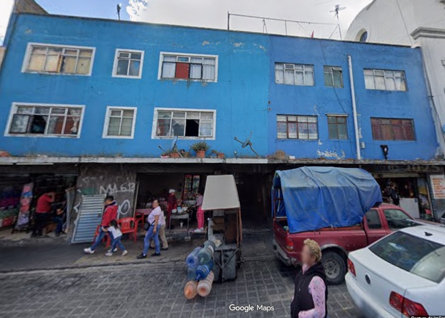 Familias caminando afuera de un edificio azul y descuidado en la ciudad de Puebla.