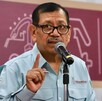 Hombre de lentes haciendo una seña con la mano mientras habla ante un micrófono.