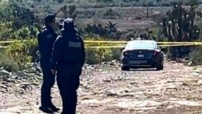 Policías observan un auto abandonado en un terreno baldío.