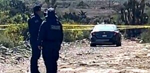 Policías observan un auto abandonado en un terreno baldío.