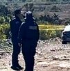 Policías observan un auto abandonado en un terreno baldío.