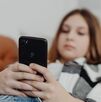 Una joven observando un teléfono celular negro mientras esta acostada