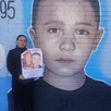 Se observa a una mujer que trae en sus manos un retrato y atrás está un mural con el rostro de un niño.