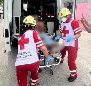Se observa a una persona que va en camilla dentro de una ambulancia, hay paramédicos y se observa a más gente en la calle.