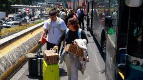 Personas caminan con maletas junto a un autobús.