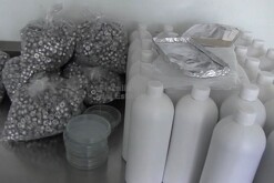 Bolsas con utensilios de química, recipientes de muestra y botellas color blanco sobre una mesa metálica