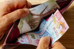 Manos de una persona abriendo una cartera con billetes mexicanos de distinta denominación