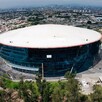 Vista aérea del exterior de la Arena Guadalajara con árboles al frente y vista de la ciudad en el fondo