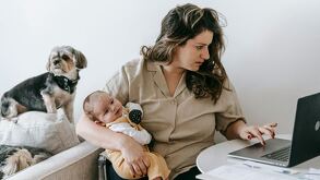 Madre con bebé en brazos mientras está trabajando en su computadora