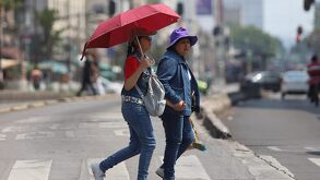 Dos personas caminan por las calles de la capital utilizando una sombrilla para protegerse del sol.