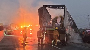 Bomberos apagan el fuego en un tráiler quemado sobre una autopista.