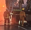 Bomberos apagan el fuego en un tráiler quemado sobre una autopista.