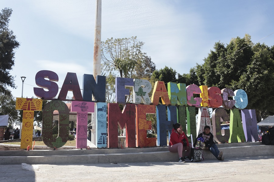 Personas sentadas junto a las letras de San Francisco Totimehuacan, en Puebla.