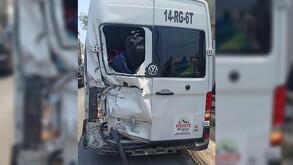 Vista de la parte de atrás de una camioneta de pasajeros blanca con la puerta izquierda aboyada y parcialmente destruida tras ser impactada por tren