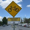 Se observa un letrero color amarillo que dice ciclovía, atrás está la calle.