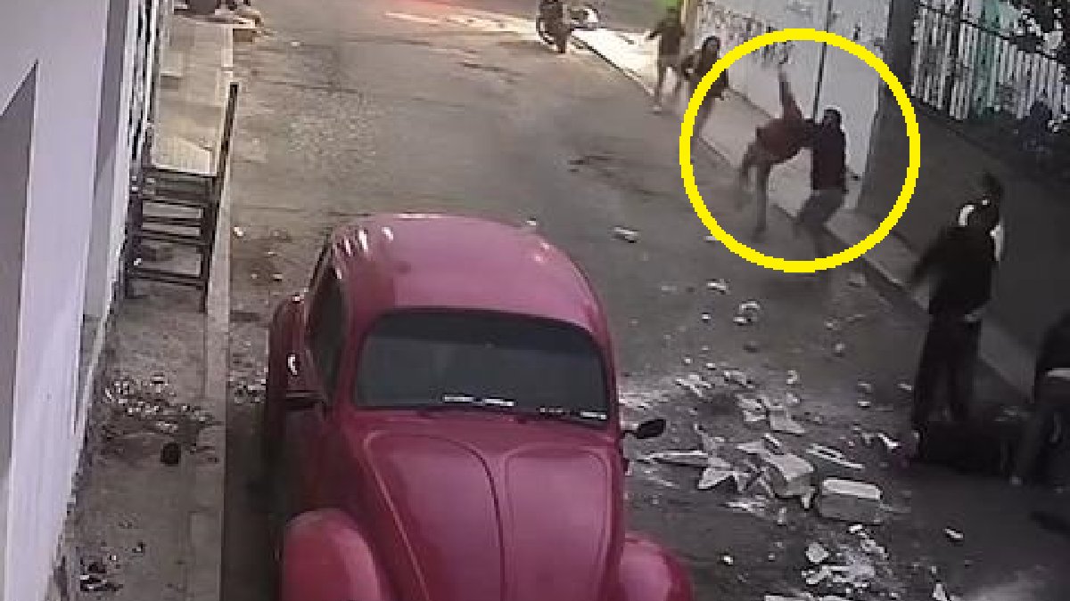 Personas en la vía pública agitando lanzando piedras hacia la parte alta de un edificio.