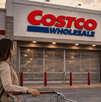 Clientes esperan frente a la entrada cerrada de una tienda Costco con un carrito de compras.