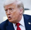 Donald Trump interactuando con alguien. El presidente habla mientras porta un traje azul con un pin de la bandera de los Estados Unidos.