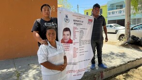 Se observa a una mujer y un hombre con un cartelón en las manos de un chico desaparecido.