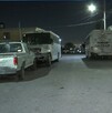 Se observa que es de noche, hay unos autos estacionados en la vía pública.