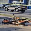 Motocicleta color naranja con negro destrozada y tendida sobre el pavimento en un área acordonada con una agente de la Policía Vial a un costado