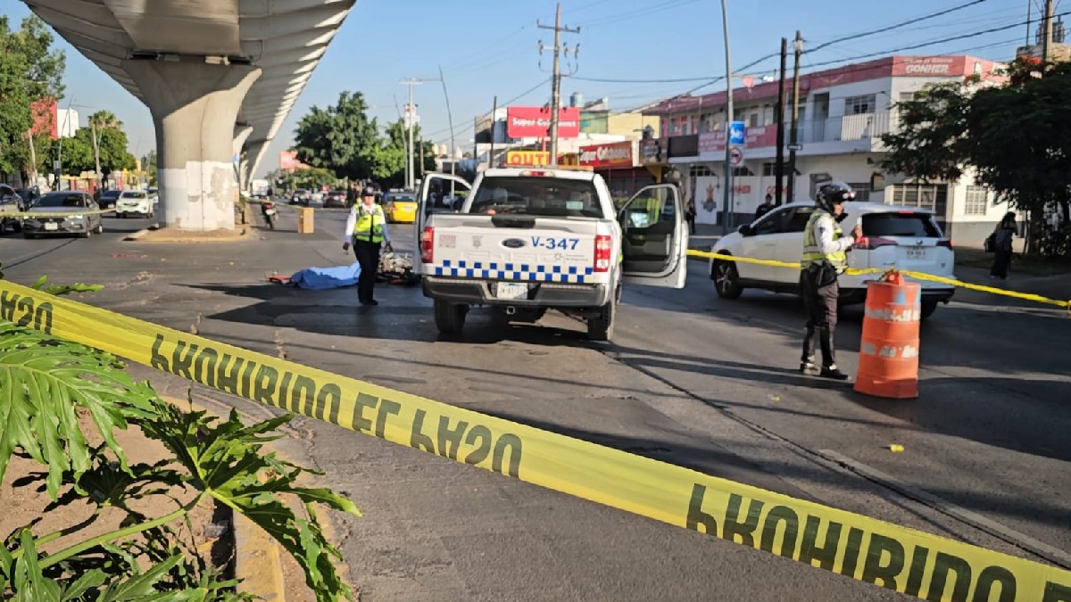 Patrulla y oficiales de la Policía Vial de Guadalajara en un área acordonada con un cuerpo cubierto por una manta azul y una motocicleta sobre la calle