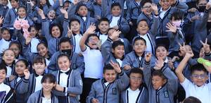 niños con uniforme escolar sonriendo y saludando a la cámara en una foto grupal