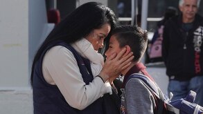 Mujer besa a su hijo antes de dejarlo en la escuela.