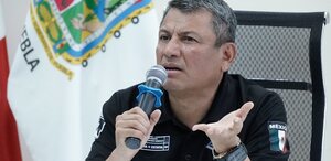 Hombre serio hablando ante un micrófono con la mano estirada.