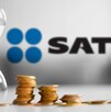 Reloj de arena blanca con pilas de monedas al lado y el logo del SAT desenfocado en el fondo