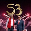 Rector de la UPAEP abrazando a otro, con el logo 53 arriba de su cabeza y fuegos artificiales