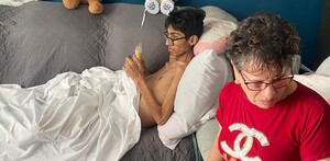 Joven acostado en sillón y al lado una señora con playera roja