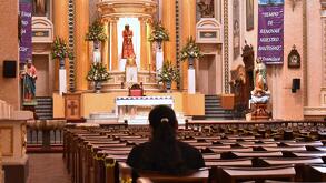 Persona reza adentro de una iglesia rodeada de santos