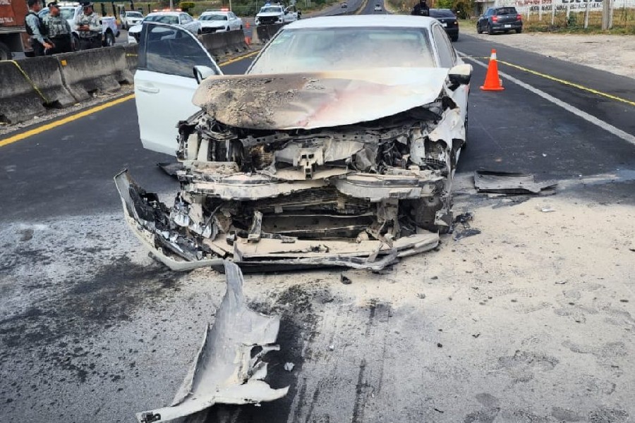 Automóvil blanco destruido y calcinado de la parte de enfrente en medio de una carretera de Tala con patrullas y policías alrededor