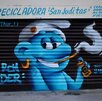 Mural de un Pitufo (fumando y con una lata de aerosol) plasmado sobre la cortina metálica de la 