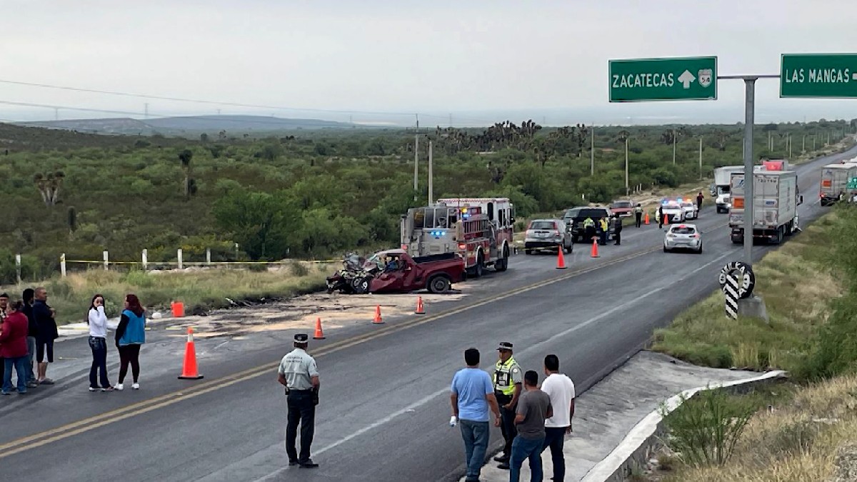 Se observan a varias personas y una camioneta destrozada del frente, en la carretera.