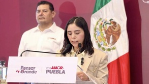 Mujer de camisa blanca leyendo un documento junto al gobernador de Puebla, Alejandro Armenta.
