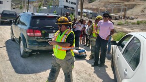 Se observa a varias personas y a un niño que lo están cargando en brazos, hay unas camionetas.