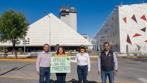 Maestros frente al Centro Expositor deseando con un cartel de feliz día del maestro