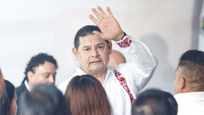 Hombre de camisa blanca alzando la mano junto a una multitud de personas.