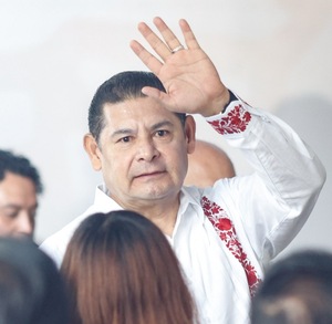 Hombre de camisa blanca alzando la mano junto a una multitud de personas.