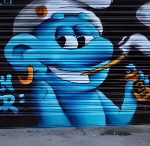 Mural de un Pitufo (fumando y con una lata de aerosol) plasmado sobre la cortina metálica de la 