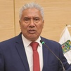 Hombre anciano vestido de traje hablando ante un micrófono.
