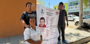 Se observa a una mujer y un hombre con un cartelón en las manos de un chico desaparecido.