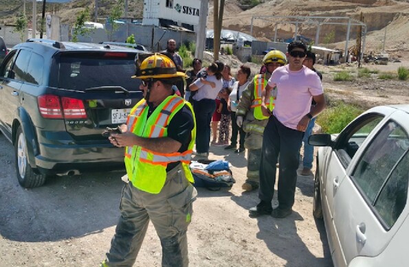 Se observa a varias personas y a un niño que lo están cargando en brazos, hay unas camionetas.