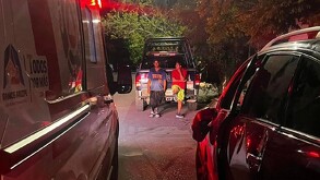 Se observa a dos hombres parados recargados en una vehículo.