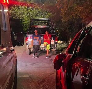 Se observa a dos hombres parados recargados en una vehículo.